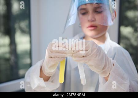 Détails: Mains d'un choolboy intelligent, tenant des tubes à essai avec des produits chimiques et des réactifs, conduite d'expérience en laboratoire Banque D'Images