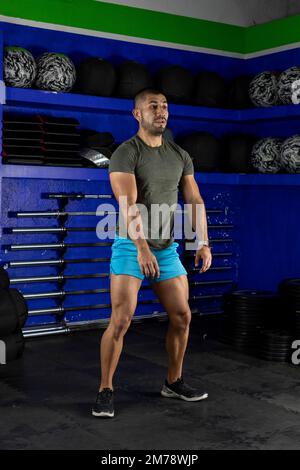 image verticale d'un homme latin faisant des squats, portant des vêtements de sport dans une salle de sport crossfit Banque D'Images