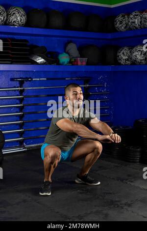 image verticale d'un homme latin faisant des squats, portant des vêtements de sport dans une salle de sport crossfit Banque D'Images