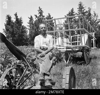 Agriculteur, ouvrier agricole, ouvrier ou paysan français pose sur tracteur avec chariot de foin, chariot ou Haywain en arrière-plan Provence France. Photo noir et blanc ou monochrome vintage de 1943 Banque D'Images