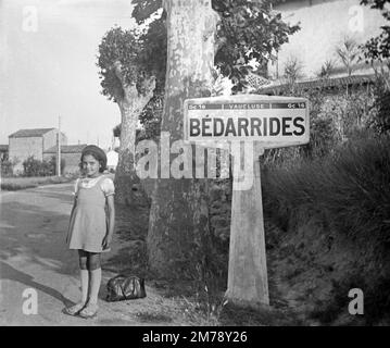 Jeune fille française à Beret & 1940s la mode ou les vêtements pose à côté d'un village signe de Bédarrides dans le Vaucluse Provence France. Photo noir et blanc ou monochrome vintage 1943 Banque D'Images