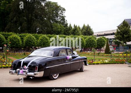 Vue arrière d'une voiture d'époque dans un jardin. La voiture est décorée de fleurs et de rubans. Une voiture d'époque est décorée et prête à prendre la mariée Banque D'Images