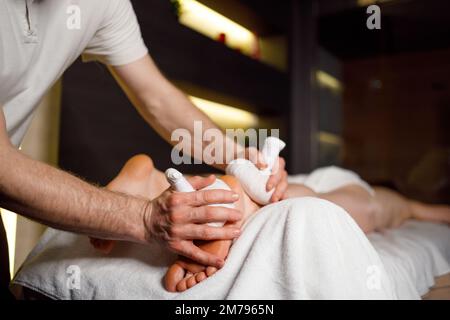 Masseuse masculine effectuant un massage des pieds avec des sacs aromatiques à base de plantes pour sa patiente dans le salon de spa Banque D'Images