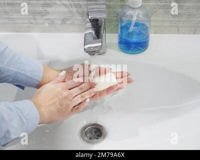 lavage des mains avec du savon ou du gel sous l'eau courante dans le lavabo, propreté et hygiène, mains de femme vêtues de chemise bleue Banque D'Images