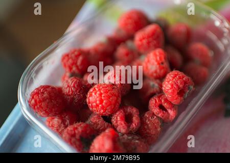Gros plan d'un récipient en plastique avec des framboises en mauvais état. Couleur rouge vif Banque D'Images