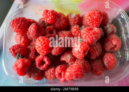 Récipient en plastique avec framboises en mauvais état, couleur rouge vif Banque D'Images