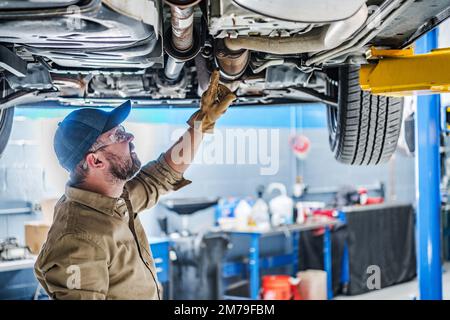 Mécanicien caucasien professionnel debout sous le véhicule soulevé au levage de voiture contrôle de l'état du convertisseur catalytique. Thème automobile. Banque D'Images