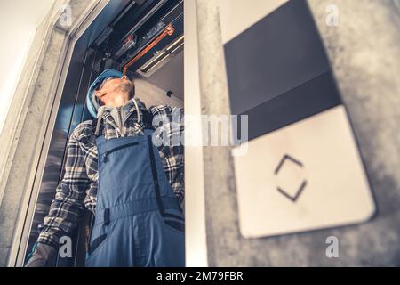 Technicien d'ascenseur professionnel caucasien qui fixe les portes de levage dans un bâtiment résidentiel nouvellement construit. Entretien de la machine de levage. Banque D'Images