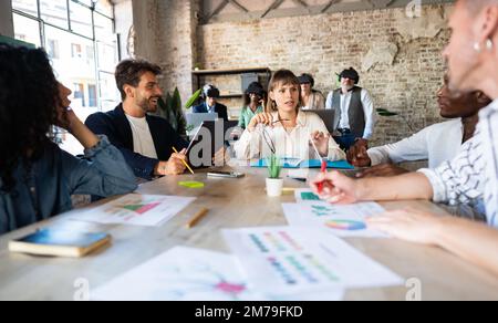 Un jeune groupe de créatifs discute des nouveaux projets numériques et du marketing numérique. À l'arrière de la salle, un groupe de collègues interagissent dans le met Banque D'Images