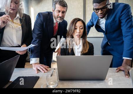 Groupe d'hommes d'affaires multiraciaux travaillant sur un ordinateur portable à une table dans un bureau et discutant de la nouvelle tendance des marchés financiers Banque D'Images