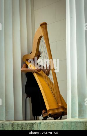 Harpiste femelle solitaire, jouant sa harpe entre les colonnes de la réplique du Temple d'Hephaestus dans le Volksgarten à Vienne, Autriche. Banque D'Images