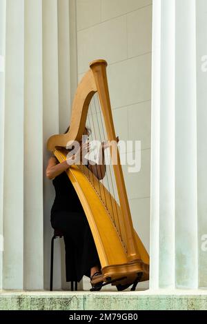 Harpiste femelle solitaire, jouant sa harpe entre les colonnes de la réplique du Temple d'Hephaestus dans le Volksgarten à Vienne, Autriche. Banque D'Images