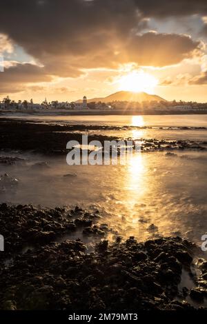 Coucher de soleil à la mer, rochers de lave longue exposition, avec vue sur la ville et la ligne d'horizon de Corralejo, Fuerteventura, îles Canaries, Espagne Banque D'Images