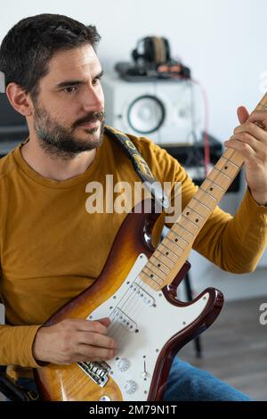 Jeune garçon avec la barbe jouant de la guitare à la maison avec le piano sur le dos Banque D'Images