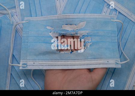 Un masque médical bleu utilisé (brûlé) dans une main contre le fond de nouveaux masques (non utilisés). Le concept de la fin de la pandémie. Zéro covid Banque D'Images