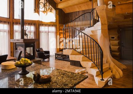 Comptoir îlot de quartz, foyer au gaz propane et escaliers en bois blanchi avec balustrade en fer forgé noir dans le salon à l'intérieur de la luxueuse maison en rondins. Banque D'Images