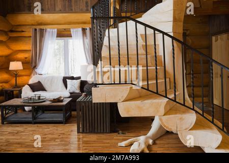 Table basse en bois noir et brun, canapé et escaliers en bois blanchi avec balustrade en fer forgé noir dans le salon à l'intérieur de la luxueuse maison en rondins. Banque D'Images