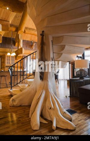 Arbre en bois blanchi et escaliers en rondins avec balustrade en fer forgé noir dans le salon et vue sur la cuisine à l'intérieur de la luxueuse maison en rondins de style scandinave. Banque D'Images