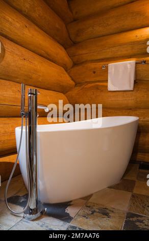 Baignoire blanche ovale autoportante dans la salle de bains avec carrelage en céramique dans la luxueuse maison en rondins de style scandinave. Banque D'Images