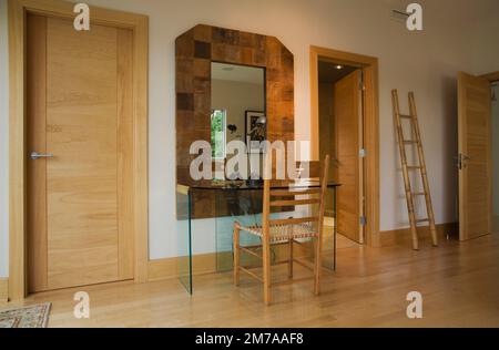 Bureau en verre et chaise ancienne en cuir brut tissée à haut dossier en bois et échelle décorative dans la chambre principale à l'intérieur de la maison de style cubiste moderne. Banque D'Images