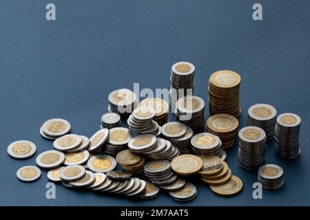 Pièces de monnaie en peso mexicain, empilées et dispersées sur une surface bleue, avec espace pour les copies. Banque D'Images