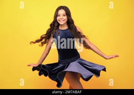 Visage de fille heureux, émotions positives et souriantes. Jeune adolescent gracieux enfant dans la mode robe isolée sur fond jaune. Robe de mouvement de jeune Banque D'Images