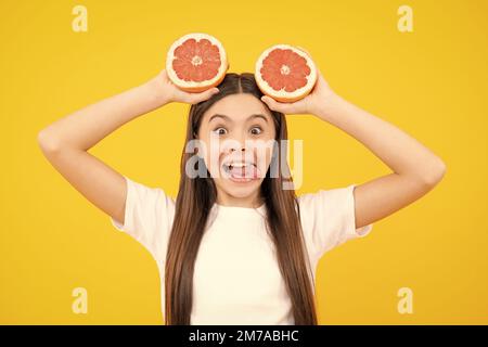 Visage amusant. Adolescente portant un pamplemousse sur fond jaune. Banque D'Images