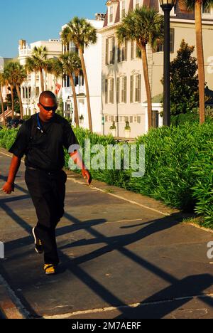 Un jeune homme marche le long d'un chemin sur le front de mer de Charleston en face des maisons historiques et des palmiers Banque D'Images