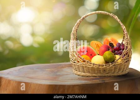 Fruits frais assortis sur fond de verdure floue, tranches de fruits dans un panier sur une table en bois dans le jardin Banque D'Images