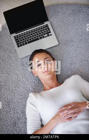 So easy it almost works itself. a young woman lying on a rug next to a laptop. Stock Photo