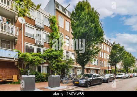 un complexe d'appartements aux pays-bas, avec des voitures garées dans la rue et des arbres bordant le bâtiment Banque D'Images