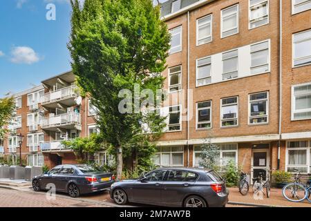 deux voitures garées sur le côté d'une rue en face d'un immeuble d'appartements avec de nombreuses fenêtres et balles Banque D'Images