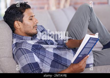 Lecture et détente. un jeune homme lisant un roman tout en se relaxant sur le canapé à la maison. Banque D'Images