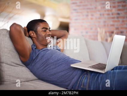 Démonstration de la bonne façon de se détendre. un beau jeune homme utilisant son ordinateur portable tout en se relaxant à la maison. Banque D'Images