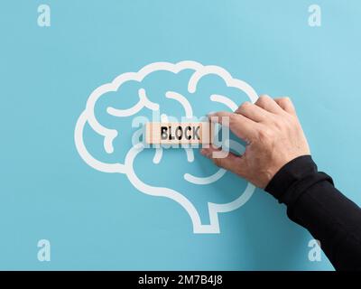 Concept de bloc mental. Supprimer ou générer des blocs mentaux de l'esprit humain. Main met un bloc de bois avec le mot bloc sur un symbole de cerveau humain. Banque D'Images