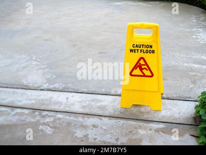 Attention jaune sol glissant mouillé avec icône d'avertissement de personne glissante sur fond de sol mouillé en béton après avoir plu avec l'espace de copie. Banque D'Images