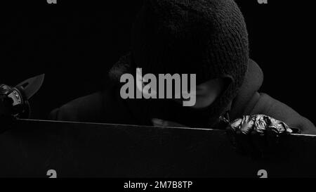 Une femme masquée cambrioleur en gants noirs regarde au-dessus d'une clôture. Concept de crime Banque D'Images