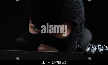 Une femme masquée cambrioleur en gants noirs regarde au-dessus d'une clôture. Concept de crime Banque D'Images