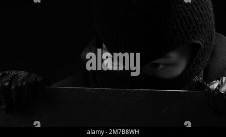 Une femme masquée cambrioleur en gants noirs regarde au-dessus d'une clôture. Concept de crime Banque D'Images