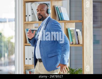 Musique, danse et écouteurs avec un directeur d'affaires noir dansant dans son bureau au travail. Le bien-être, la radio et la liberté avec un travailleur masculin senior Banque D'Images