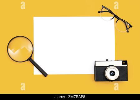 Arrière-plan minimal avec papier vierge, appareil photo et loupe, pose à plat. Banque D'Images