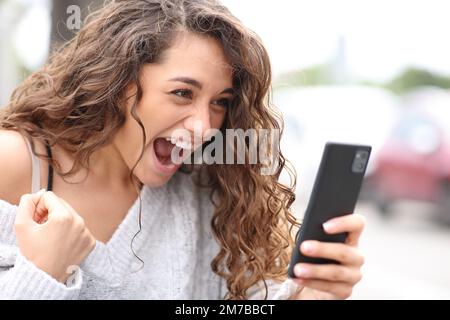 Une femme excitée qui célèbre son téléphone dans la rue Banque D'Images