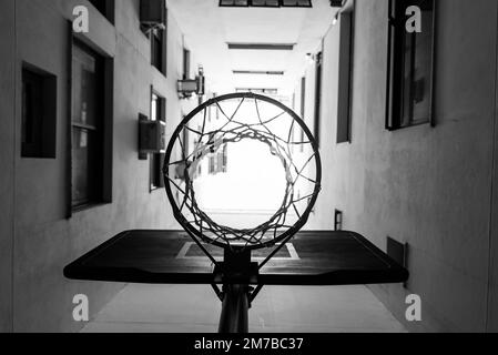 Photo en niveaux de gris à faible angle d'un panier de basket-ball contre un bâtiment résidentiel. Banque D'Images