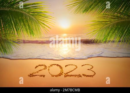 Accueillant l'écriture manuscrite de l'année 2023 sur plage de sable et feuille de noix de coco, concept du nouvel an à venir heureux. Banque D'Images