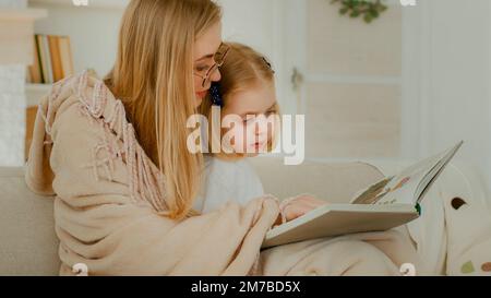 Petite petite fille caucasienne enfant fille enfant enfant bébé avec mère dans le salon lecture littérature regardant l'album photo maman lire livre montrant Banque D'Images