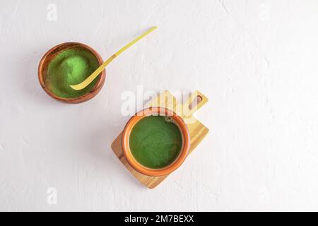 Vue de dessus du thé vert matcha fraîchement préparé dans une tasse en céramique et de la poudre de matcha dans un bol en bois avec une cuillère à mesurer en bambou. arrière-plan blanc Banque D'Images