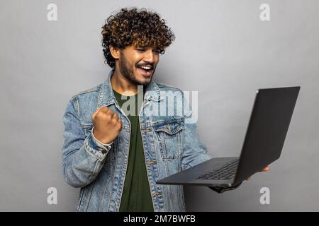 Portrait d'un homme d'affaires barbu enthousiaste criant avec joie et tenant un ordinateur portable, se réjouissant de la victoire, pariant en ligne, portant un costume de style officiel. Intérieur Banque D'Images