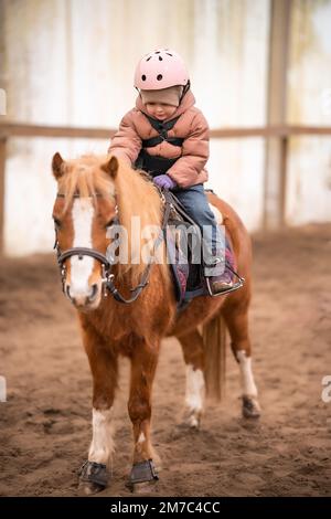 Leçon de équitation pour les petits enfants. Une jeune fille de trois ans fait du poney et fait des exercices Banque D'Images