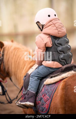 Leçon de équitation pour les petits enfants. Une jeune fille de trois ans fait du poney et fait des exercices Banque D'Images