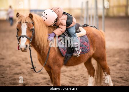 Leçon de équitation pour les petits enfants. Une jeune fille de trois ans fait du poney et fait des exercices Banque D'Images